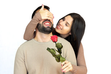Young girl surprising her partner by covering his eyes with her hand while giving him a rose.