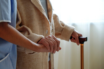 Senior woman holding quad cane handle in elderly care facility. Hospital nurse taking care of...