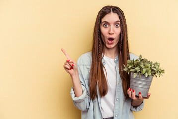 Young caucasian woman holding a plant isolated on yellow background pointing to the side