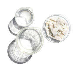 Calcium carbonate chip in Chemical watch glass place next to crystal clear liquid in beaker. Closeup chemical ingredient on white laboratory table. Top view