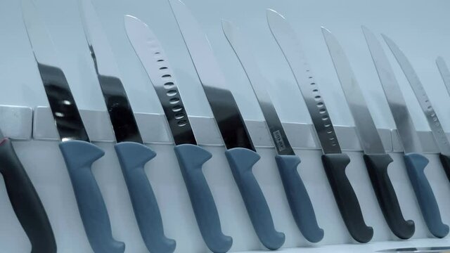 A row of new sharp shiny knives with black and blue plastic handles hanging from a magnetic tape on the wall. Shot in motion. Closeup