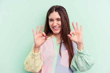Young caucasian woman isolated on green background cheerful and confident showing ok gesture.