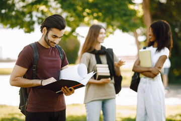 Three international students standing in a park and holding a books