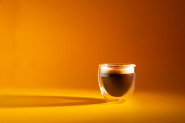 Freshly brewed creamy espresso in a glass coffee cup isolated on yellow background, close up with copy space - obrazy, fototapety, plakaty