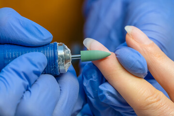 Manicure master in blue gloves grinds nails with a special device before coating gel polish, macro.