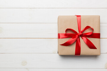 Holiday gift box wrapped in craft paper with colored bow on table background. Top view, flat lay,...