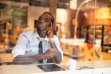 Businessman drinking coffee in cafe. Handsome African man talking to the phone while enjoying in fresh coffee