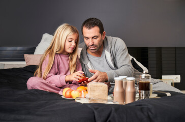 Father with daughter in pajamas having breakfast in bed. happy portrait family moments. Positive human emotions