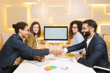 Good deal. Full length view of the firm strong handshake of business partners in office. Two female colleagues looking at this with pleasure smile