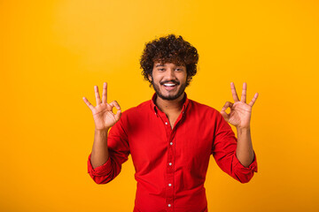 I am ok. Portrait of cheerful brown-haired man with beard and mustache in casual shirt looking at camera and showing okay hand gesture. Indoor studio shot isolated on orange background - obrazy, fototapety, plakaty