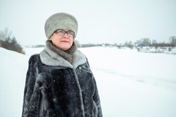 Fototapeta premium An elderly woman walks against the background of a frozen river.