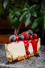 Cheesecake ai frutti di bosco guarnita con zucchero a velo e  servita su un piatto nero su un tavolo di legno di un bar