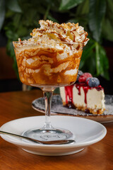 Caffè freddo al caramello servito su un tavolo di legno con una cheesecake ai frutti di bosco sullo sfondo