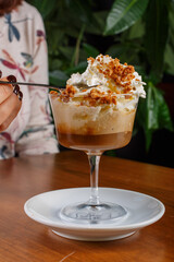 Cucchiaino che viene immerso in un Caffè freddo all'amaretto con panna montata servito su un tavolo di legno