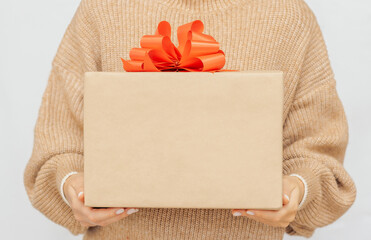 Woman's hands gift box with red ribbon, woman in warm beige jumper Hold present box with bow. Mock...