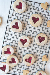 Close up image of heart shaped Linzer cookies arranged on a cooling rack. Red hearts biscuits fill the frame in flat lay top down view. Love, romance and valentines day food concept with copy space