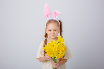 Obraz na płótnie Canvas cute little girl with bunny ears holds a bouquet of yellow daffodil flowers on a white background,