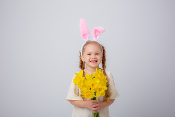 cute little girl with bunny ears holds a bouquet of yellow daffodil flowers on a white background,