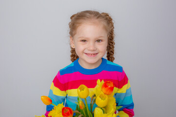 a cute little girl in a multicolored sweater holds a bouquet of spring flowers on a white background