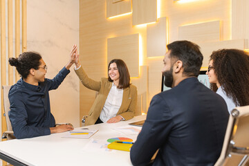 Cheerful men giving high five to his pretty female colleague. Another members of team looking at them and smiling. Stock photo