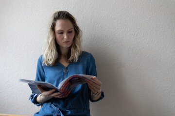 Junge Frau vor heller Wand liest eine Zeitschrift