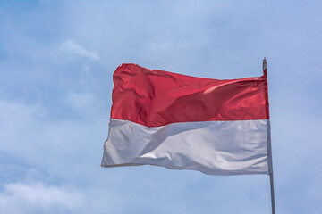 Fototapeta na wymiar Indonesian red and white national flag rising and under the clear and bright blue sky