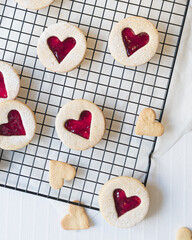 Close up image of heart shaped Linzer cookies arranged on a cooling rack. Red hearts biscuits fill the frame in flat lay top down view. Love, romance and valentines day food concept with copy space