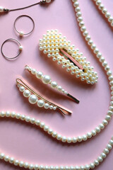 Various pearl jewelry and hair accessories on pink background. Flat lay.