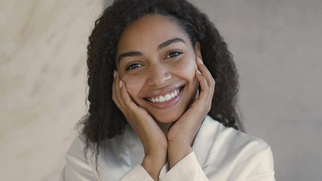 Natural beauty concept. Close up of young positive african american lady smiling at camera, touching her smooth cheeks