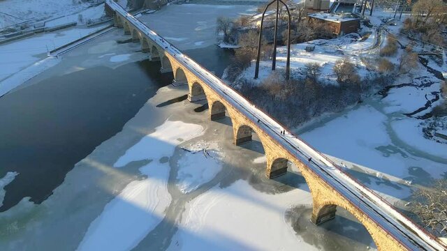 Aerial view of Mississippi river frozen on a winter afternoon and people crossing at stone Arch near Minneapolis downtown