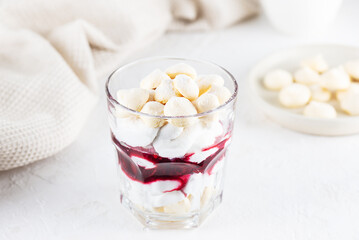 Homemade vegan dessert with meringue, coconut cream and cherries in a glass on a light table. Sugar, gluten and lactose free.