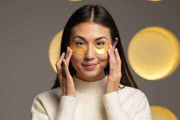 Young Asian woman with clear radiant skin with moisturizing golden patches under her eyes