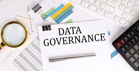 DATA GOVERNANCE text on the white paper on the light background with charts paper ,keyboard and...