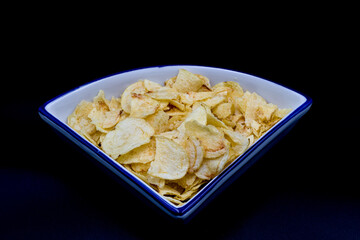 Potato chips in a triangular white-blue plate isolated on a black background