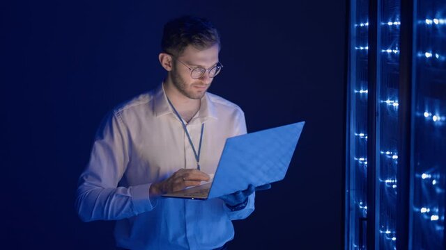 Male Server Engineer in Data Center. IT engineer inspecting a secure server cabinet using modern technology laptop coworking in data center.