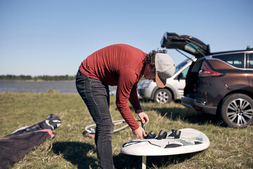 Windsurfer and camper packing and unpacking from a car in nature.