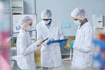 Group of scientist in lab coats using tablet pc and making notes in medical card while doing research in hospital laboratory