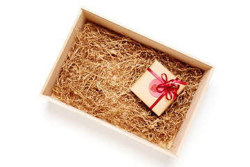 Wooden box with present wrapped in brown craft paper with red ribbon, filled with paper filler, top view