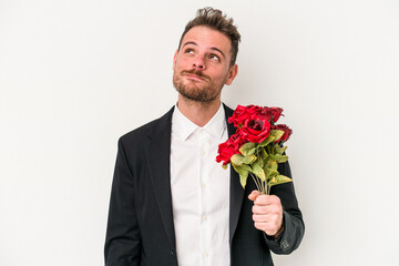 Young caucasian man holding bouquet of flowers isolated on white background dreaming of achieving goals and purposes