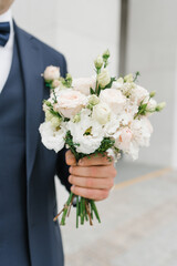 The groom in a blue suit holds in his hand a delicate wedding bouquet for his beloved bride