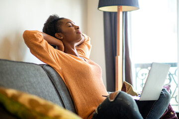 young woman relaxing at home with hands behind head and eyes closed