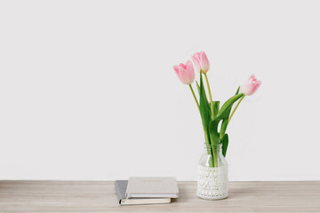 A bouquet of pink tulips of spring flowers in a vase stands on the desktop near the notebooks. Copy space