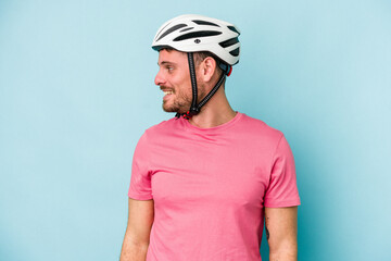 Young caucasian man with bike helmet isolated on blue background looks aside smiling, cheerful and pleasant.