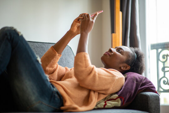 Young Black Woman Relaxing At Home On Sofa Looking At Mobile Phone