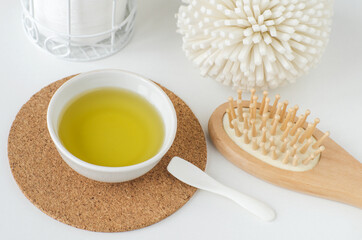 Small white bowl with olive (coconut, castor) oil and wooden hairbrush. Homemade skin and hair...