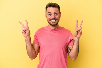 Young caucasian man isolated on yellow background showing victory sign and smiling broadly.