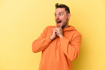 Young caucasian man isolated on yellow background praying for luck, amazed and opening mouth looking to front.