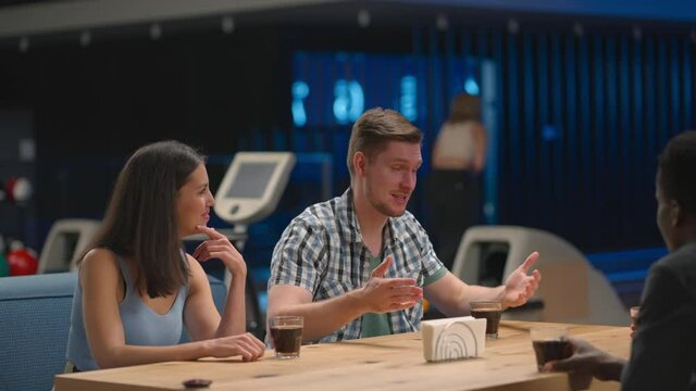 A multi ethnic group of friends in a bowling club are chatting at the table and smiling