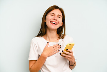 Young English woman holding mobile phone isolated on blue background laughs out loudly keeping hand on chest.