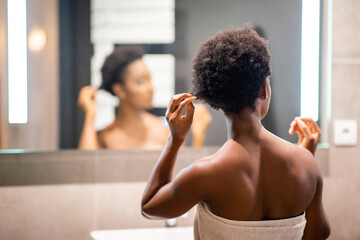 behind young black woman adjusting hair and looking in mirror